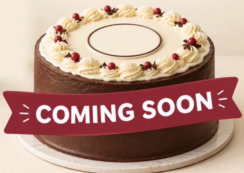 A chocolate celebration cake with cream piping and red berries, with a Coming Soon ribbon across the front